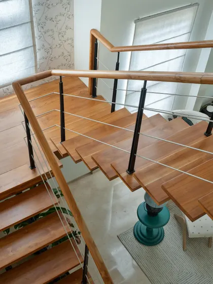 A top-down view of the 'House of Kismish' staircase, showing the warm wooden steps and sleek metal and wire railing.