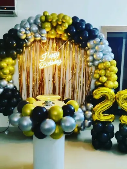 A popular choice for milestone birthdays, this 25th birthday setup includes a full ring backdrop with black, gold, and silver balloons. It's paired with a cake pedestal and foil number balloons on columns.