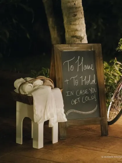 A thoughtful detail for guests at an evening outdoor event: a basket of shawls with a sign that reads "To Have & To Hold In Case You Get Cold!"