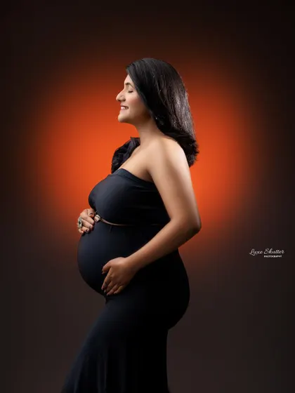 A classic profile shot in a timeless black gown. The warm back-light creates a beautiful halo effect, highlighting the silhouette of the mother-to-be.