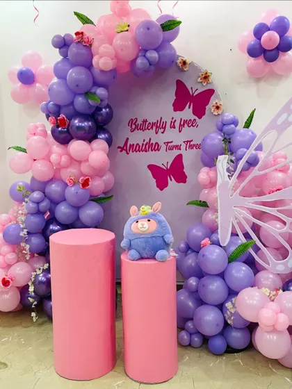"Butterfly is free, Anaisha turns three!" This adorable butterfly-themed party features a purple and pink balloon arch on a custom backdrop, with large butterfly wing props for photos.