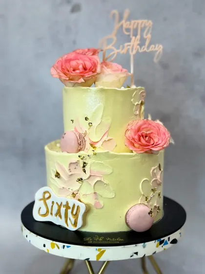 A beautiful two-tiered cake for a 60th birthday. I used a soft yellow buttercream, textured accents, and decorated it with fresh pink roses, macarons, and a touch of gold leaf.