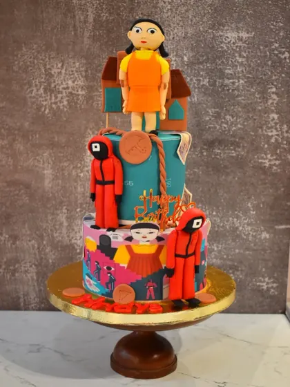 A thrilling two-tier cake based on the popular series Squid Game. It features edible figurines of the guards and the iconic doll, perfect for a fan's birthday party.