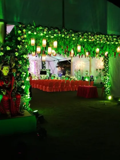 An evening event entrance illuminated with green lights, featuring floral arches and traditional statues.