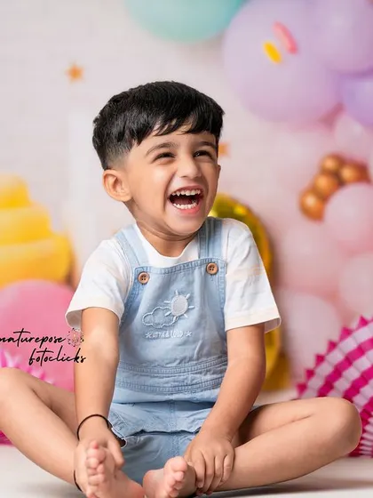 A burst of pure, infectious laughter during a third birthday shoot. The colorful candy-themed backdrop with pastel balloons and giant ice cream props makes for a fun and vibrant setting.
