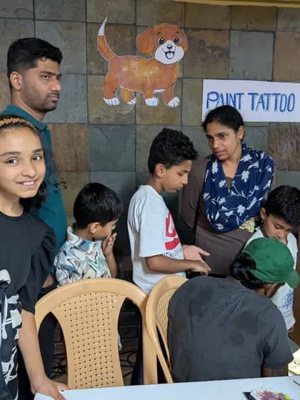 A group of children and parents gathered around the paint tattoo station. It's a great way to break the ice and create a fun, festive atmosphere at our adoption drives.