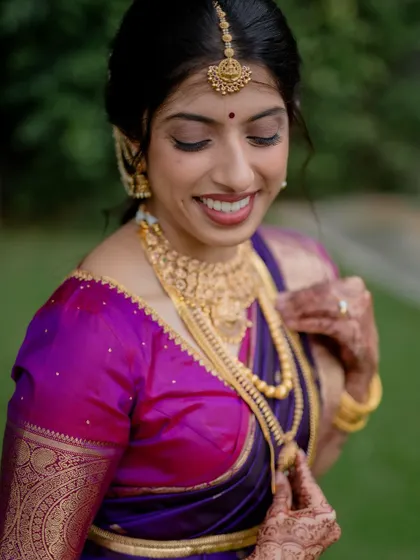 A moment of quiet reflection for the bride. Her vibrant purple and pink saree and traditional gold jewelry are beautifully highlighted in this classic portrait.