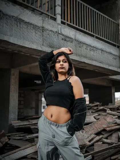A strong pose with the model's hand on her head, her crop top and cargo pants contrasting with the unfinished concrete building behind her.
