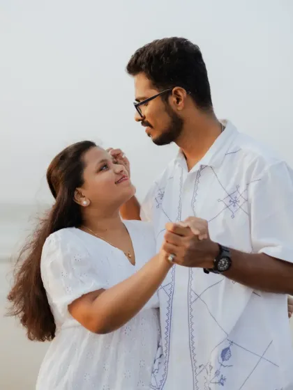 A sweet, dance-like pose between the couple during their beach photoshoot. These playful moments showcase their happy connection.