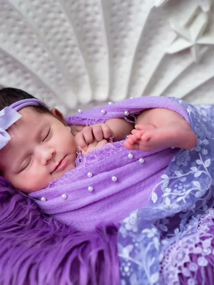A close-up of the newborn in the purple shell setup, highlighting her sweet sleeping face and the pearl details on her swaddle.