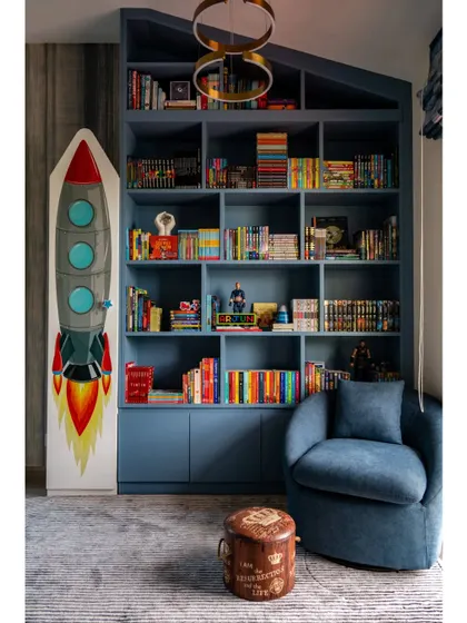 A feature on the son's room, showcasing the imaginative design. A rocket-ship themed storage unit stands next to the bold blue bookshelf, creating a space that is both playful and stylish.