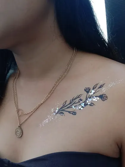 A delicate branch with small roses and leaves, trailing along the collarbone with a sprinkle of silver glitter.