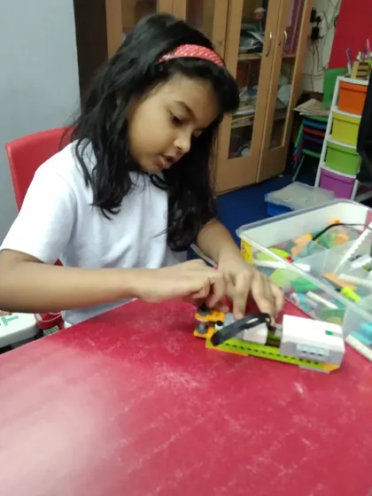A young girl concentrates on connecting a sensor to her LEGO robot, an essential step in making her creation interactive.
