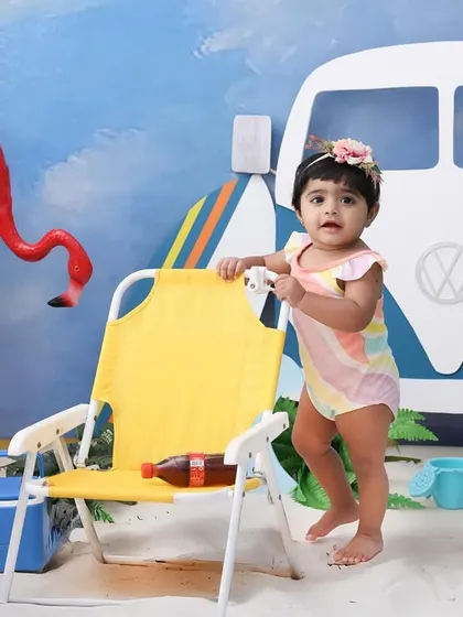 Ready to catch a wave. This little one is standing tall in our beach-themed setup. The props, like the mini surfboard and cooler, add a fun, playful touch to the scene.