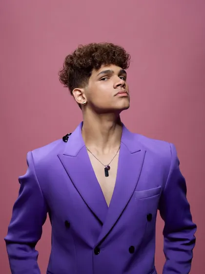 A vibrant and bold commercial headshot for a hair brand. The bright purple jacket against the pink background creates a high-energy look that is both professional and full of personality.