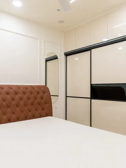 A look at the master bedroom in the Hyderabad 2BHK, showcasing a tufted leatherette headboard and a sleek sliding wardrobe with lacquered glass panels.
