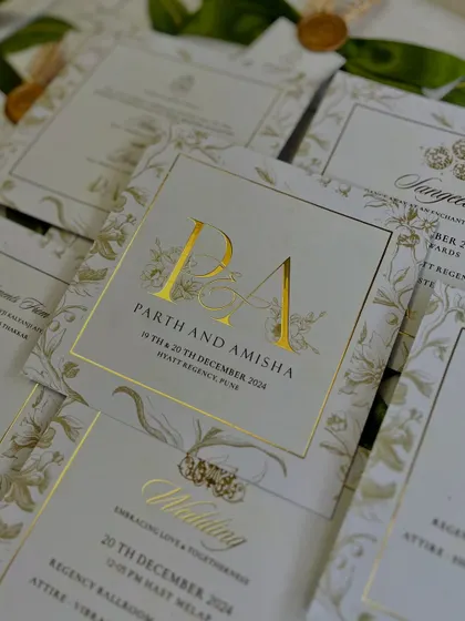 A detailed view of the invitation cards for Parth and Amisha, featuring their gold-foiled monogram. The design uses an elegant ivory and gold palette with a subtle floral border, reflecting a theme of timeless sophistication.