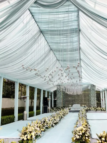 The aisle for the Anand Karaj ceremony, lined with white and blue flowers leading to the main stage. The ceiling is draped in soft, translucent fabric with hundreds of tiny hanging bells.