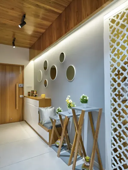 A foyer design featuring a low cabinet with a seating nook, set against a wall with decorative circular mirrors. A CNC-cut jali screen provides a partial partition.