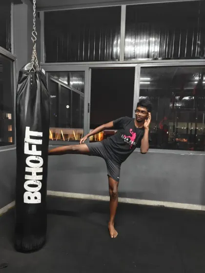 A member posing with a high kick next to the punching bag. This showcases the flexibility and power developed in our kickboxing classes.