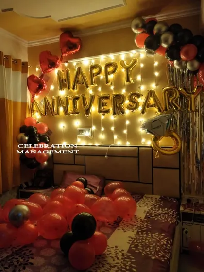 A classic anniversary surprise that never fails to impress. This bedroom decoration features "Happy Anniversary" foil balloons against a wall of fairy lights, a festive mix of red, black, and silver balloons, and a special diamond ring balloon to mark the occasion.