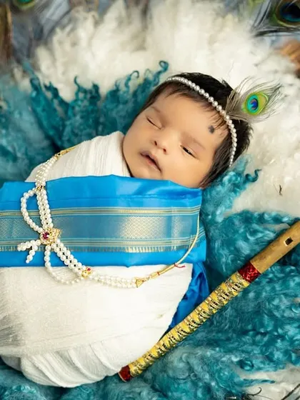 A divine newborn portrait with a 'Little Krishna' theme. The baby is peacefully swaddled and surrounded by peacock feathers, creating a stunning and artistic image.