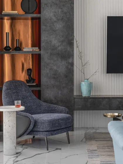 Every corner contributes to the interior design. Here, bold gold paneling in the showcase unit adds glamour, while a comfortable lounge chair and marble side table create a cozy reading spot.