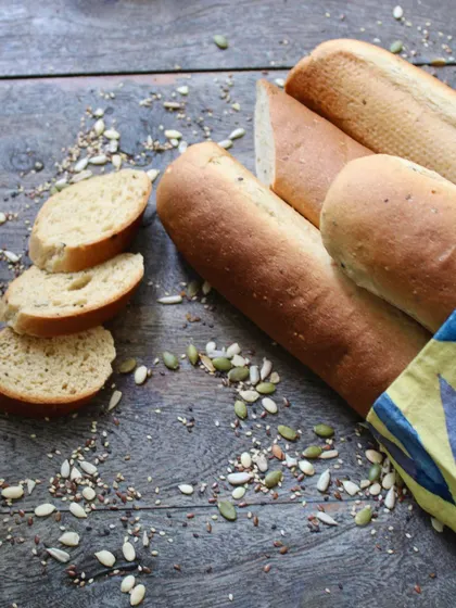 Slices of our in-house whole-wheat baguette, surrounded by the mixed seeds we use. It's simple, rustic, and delicious, perfect for our avocado toast or to enjoy on its own.