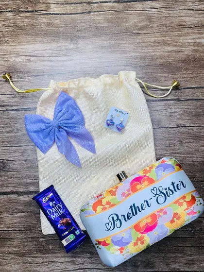 This cute Rakhi combo for a sister includes a printed clutch with a "Brother-Sister" theme, a bow clip, earrings, and a chocolate, all packed in a reusable jute potli bag.