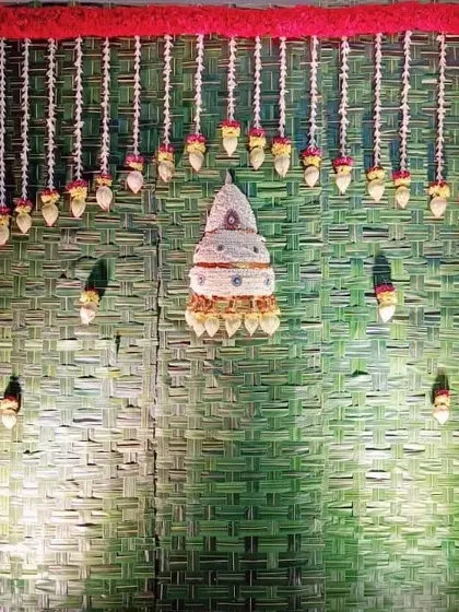 This is a full view of one of our Varamahalakshmi pooja backdrops. The design includes a woven coconut leaf mat, a red flower border, and hanging floral elements, including a traditional cone-shaped flower arrangement at the center.