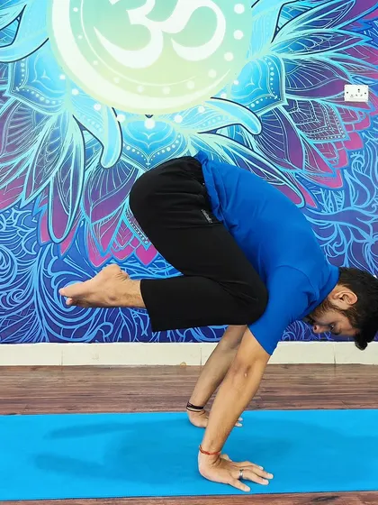 A student holds Bakasana (Crow Pose) with perfect form against our vibrant studio mural.