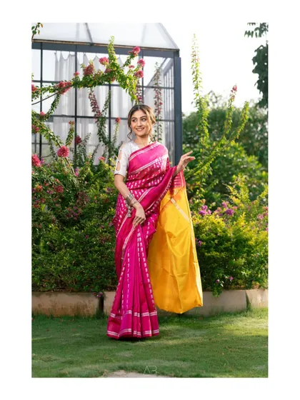 A full-length portrait of a woman in a stunning pink and yellow saree. The garden setting and her happy expression make this a bright and cheerful image.