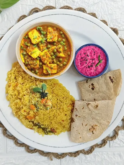 A beautifully plated meal featuring our popular Mutter Paneer, vibrant Beetroot Raita, fragrant Veg Pulao, and soft rotis. This is a perfect example of a balanced and delicious lunch.