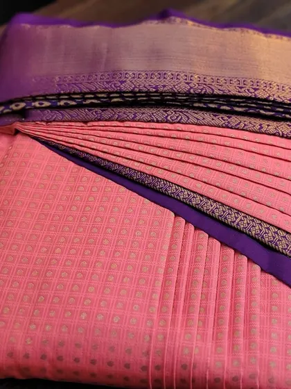 A pre-pleated client saree in a vibrant coral pink, neatly box-folded.