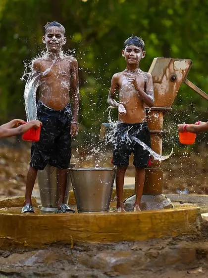 Two boys stand proudly after being splashed, while two girls prepare the next wave of water. This posed moment amidst the action shows their playful and confident spirit.