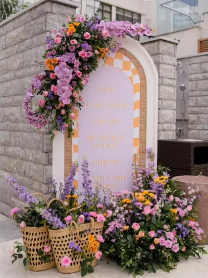 An arched welcome sign is framed by a stunning arrangement of pastel purple and yellow flowers.