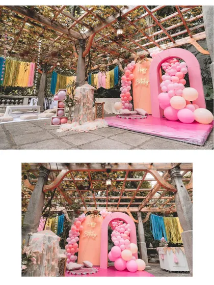A gorgeous pink-themed party setup under a pergola. The combination of balloon arches, hanging tassels, and elegant decor creates a stunning visual for a first birthday.