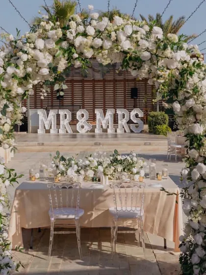 A 'Mr & Mrs' sign and a beautiful white floral arch create a classic and elegant focal point for this outdoor wedding reception.