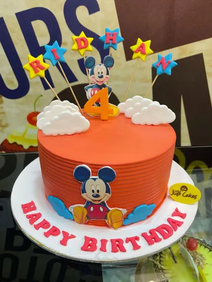 A bright orange 3kg Mickey Mouse cake with character cutouts and colorful stars.