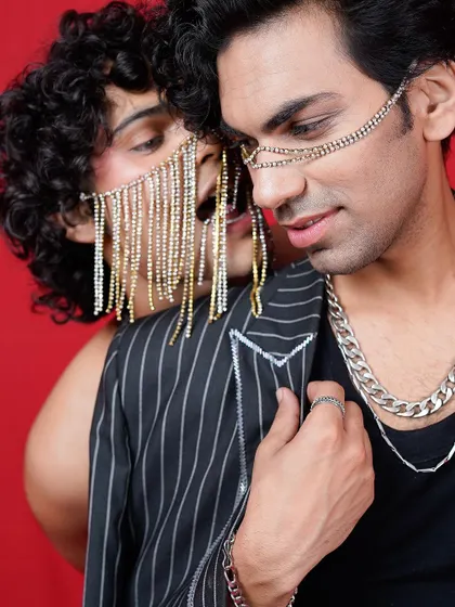 An intimate and edgy editorial shot against a bold red background. The use of chain masks and close interaction between the models creates a provocative and high-fashion narrative.
