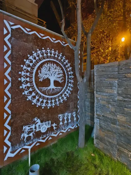 The same Tree of Life mural illuminated at night. The artificial light creates a dramatic effect, making the white figures stand out against the dark red wall and turning the art into a striking feature after sunset.