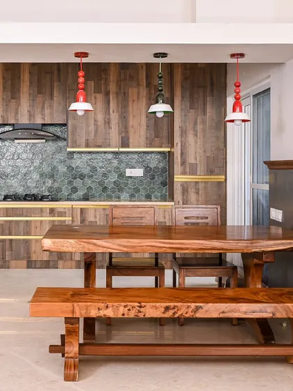 This dining space features a large, live-edge wooden table and bench, paired with a modern kitchen that has dark wood paneling and hexagonal green tiles.