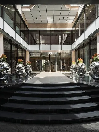 The grand entrance to The Layered Office features a new canopy and revolving door leading into an open-air courtyard, with black granite steps creating a formal approach.
