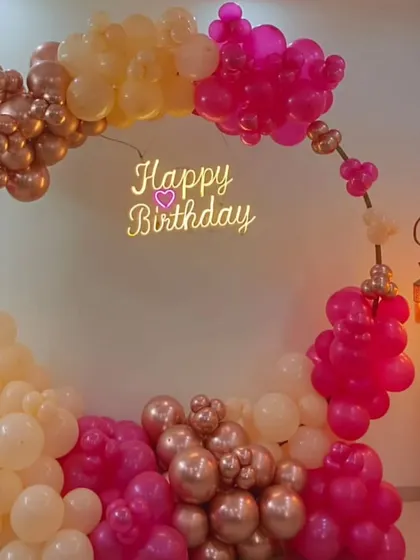 An elegant and simple circular balloon arch in soft pink, peach, and rose gold tones. The floating "Happy Birthday" neon sign adds a modern touch, making it a great backdrop for photos.