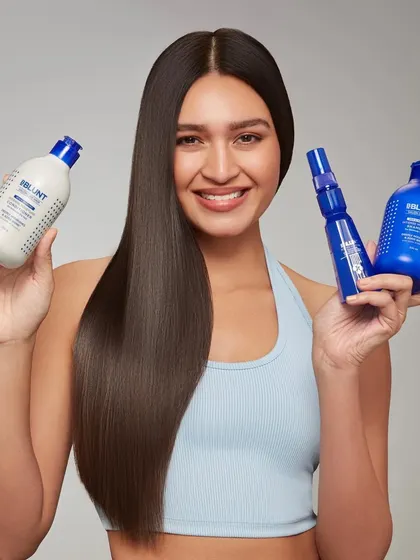 A product-centric shot for a BBlunt haircare system. The model holds a shampoo, conditioner, and serum, displaying the full range of products needed to achieve the smooth, healthy hair she is modeling.