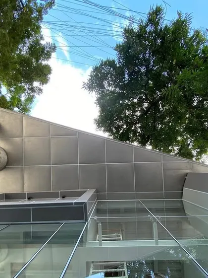 An upward view of the angled glass and steel facade of MAP, framed by the sky and trees.
