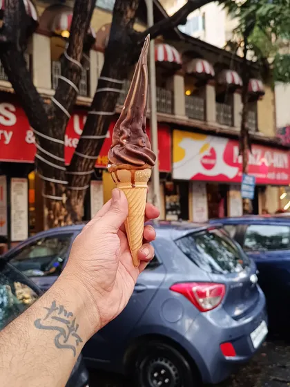 A simple, effective shot of a chocolate soft-serve ice cream cone held against a street background. It’s a relatable image that captures the joy of a simple treat.