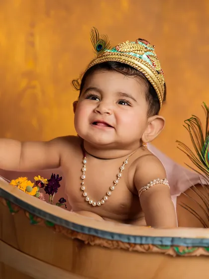 A joyful baby dressed as little Krishna, with a peacock feather crown and a happy smile. A perfect way to celebrate a milestone with a traditional theme.