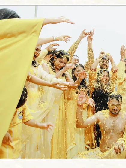 A wide shot of the Haldi celebration, showing the couple surrounded by friends and family who are all part of the fun. This captures the scale and energy of the event.