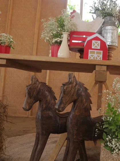 A pair of rustic wooden rocking horses stand as part of the farm-themed decor, adding a touch of nostalgic, playful charm to the barnyard setting.